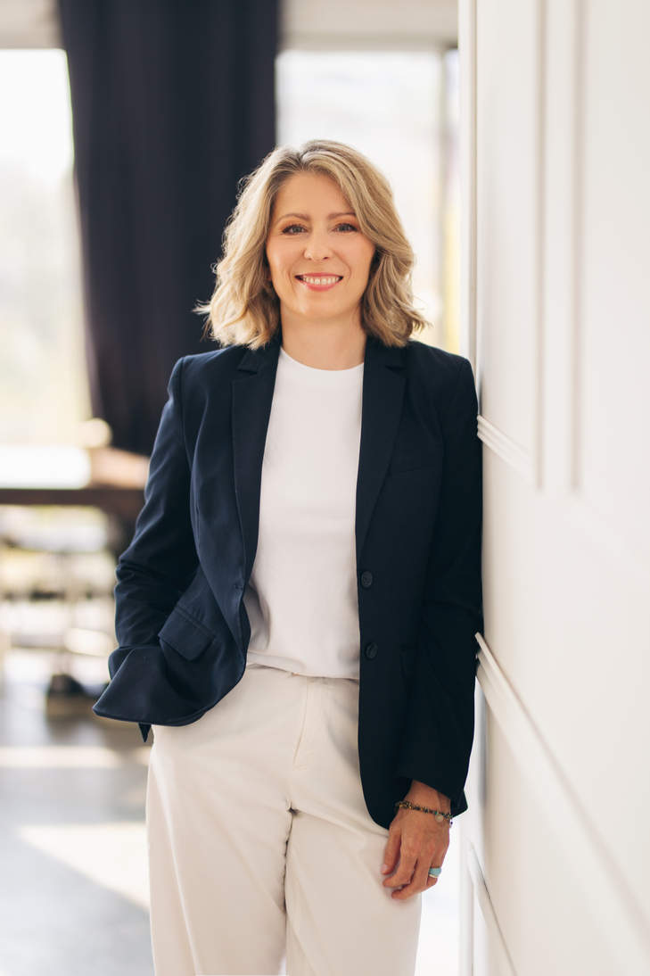 Dagmara Seliga stojąca przy jasnej ścianie, uśmiechnięta i profesjonalna – ekspertka tworząca rozwiązania rozwojowe szyte na miarę organizacji.